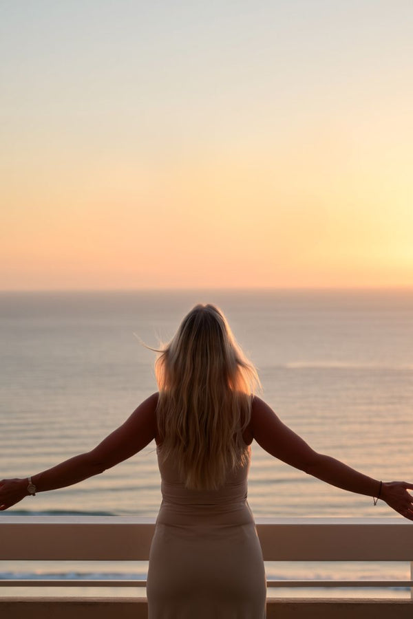 Woman standing on a balcony at sunset, overlooking the calm ocean — symbolizing healing, freedom, and emotional rebirth after heartbreak.